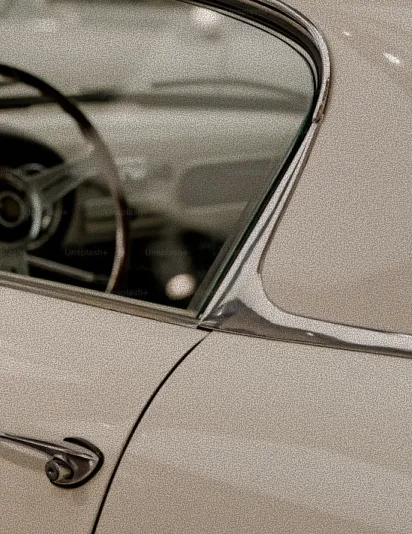 Nahaufnahme eines cremefarbenen Oldtimer-Autotürgriffs und Fensters mit sichtbarem Lenkrad im Innenraum.