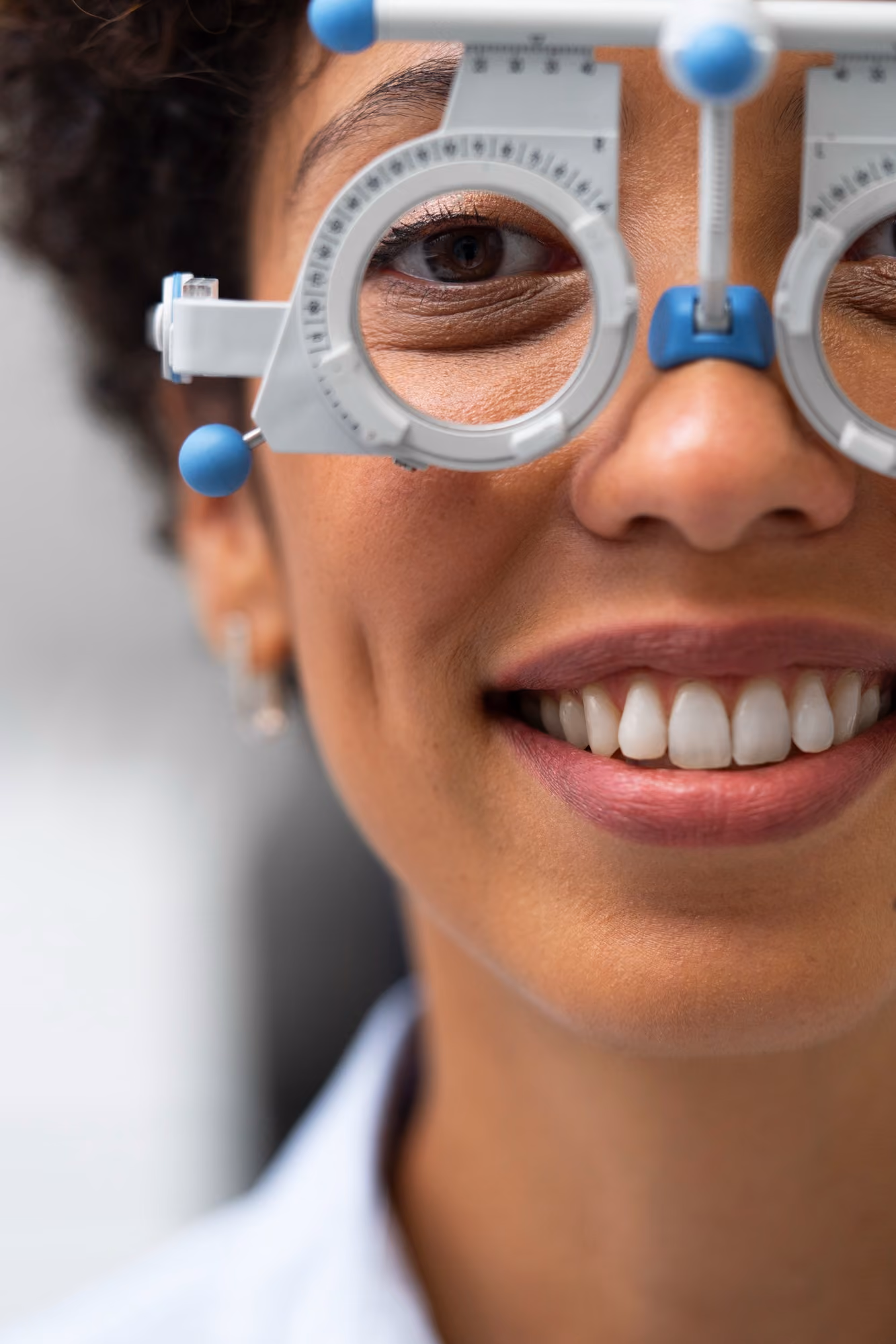 Close-up of a smiling woman wearing an eye exam device during a vision test.