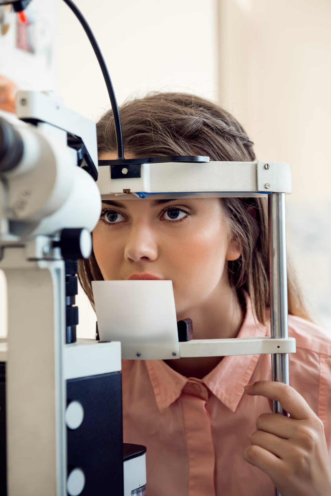 Woman in a pink shirt undergoing an eye exam using a slit lamp machine.