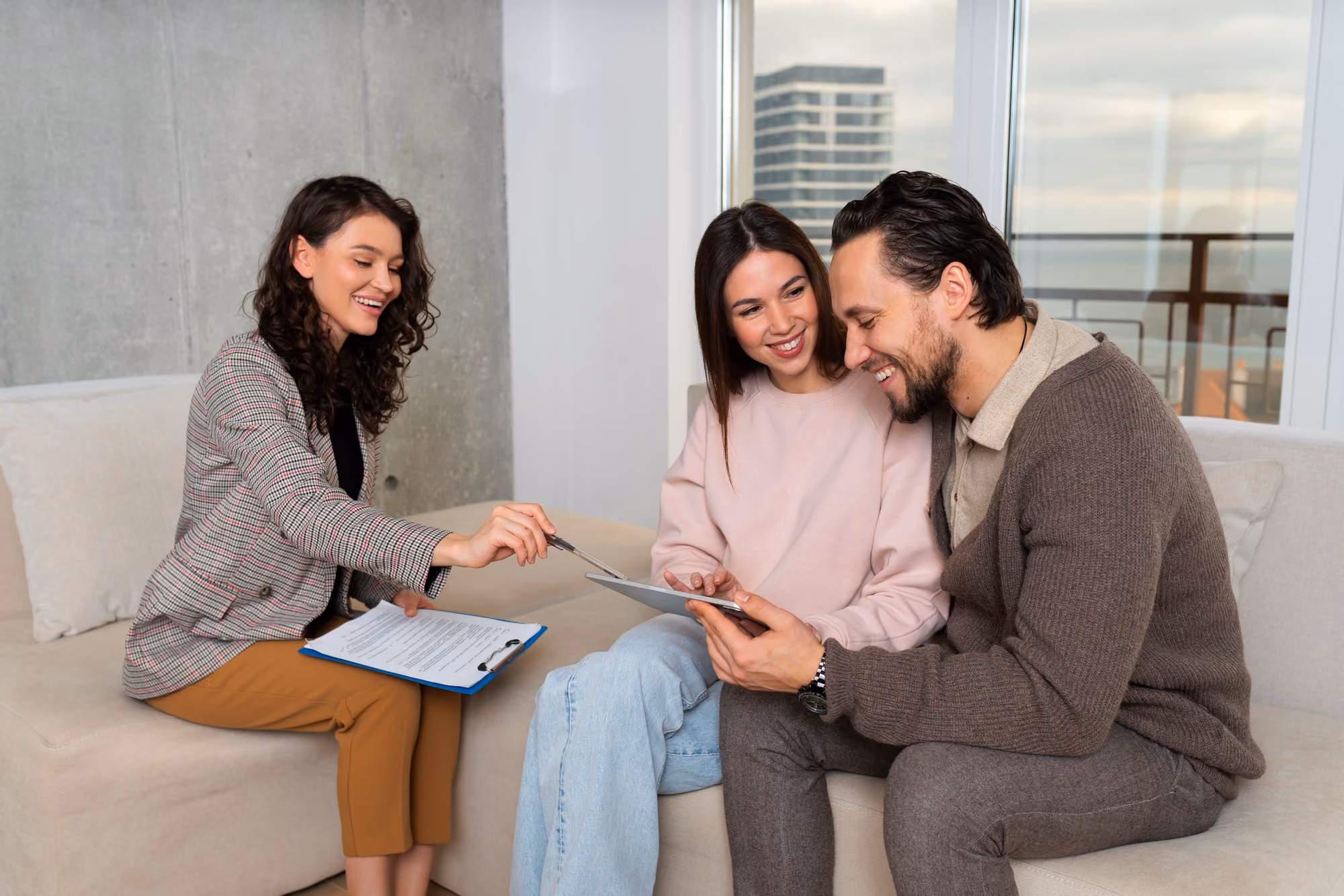 Couple sitting on sofa with a woman consultant showing documents and tablet during a meeting.