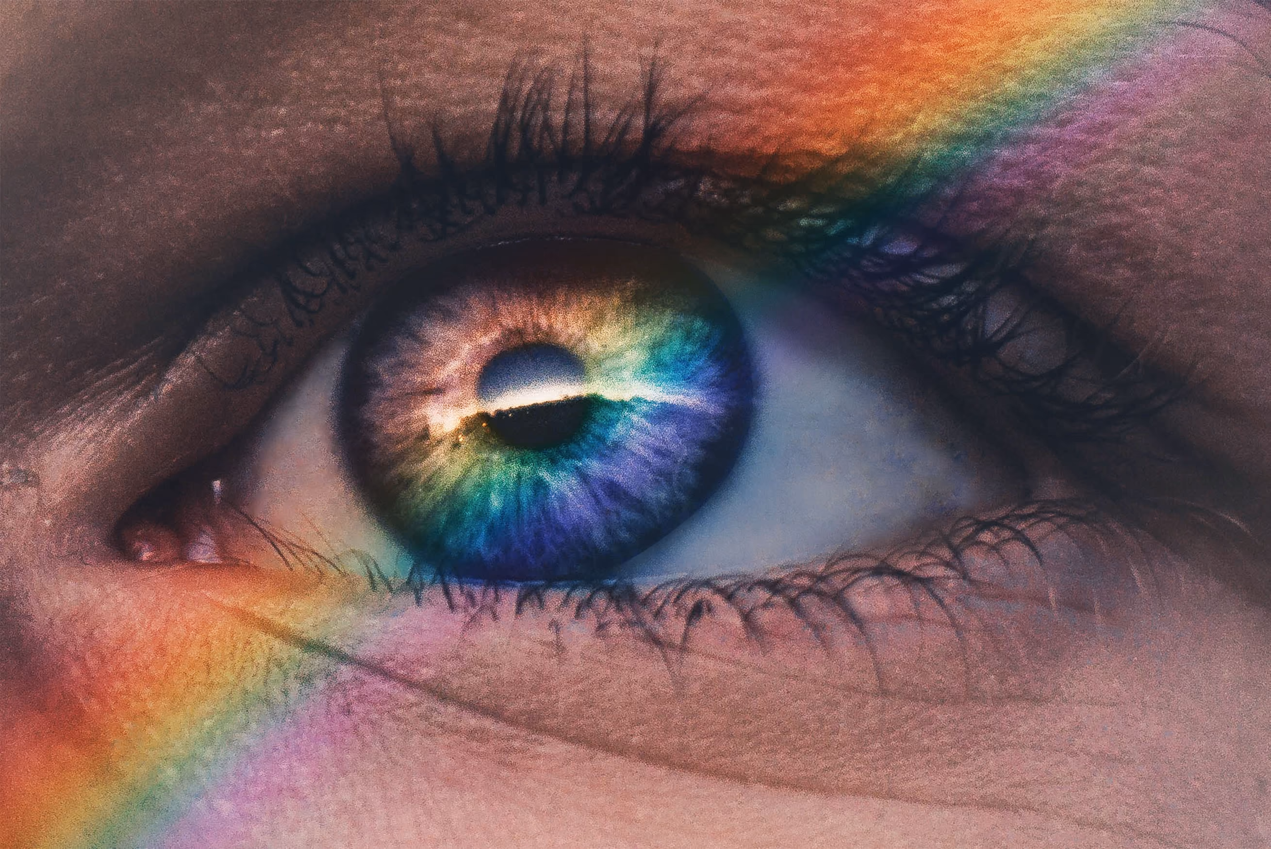 Close-up of a human eye with a vivid rainbow reflection across the iris and surrounding skin.