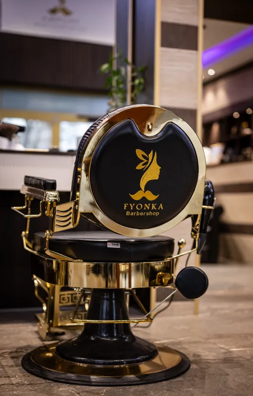Luxuriöser Friseurstuhl mit goldenem Rahmen und schwarzer Polsterung, Logo von Fyonka Barbershop auf der Rückenlehne.