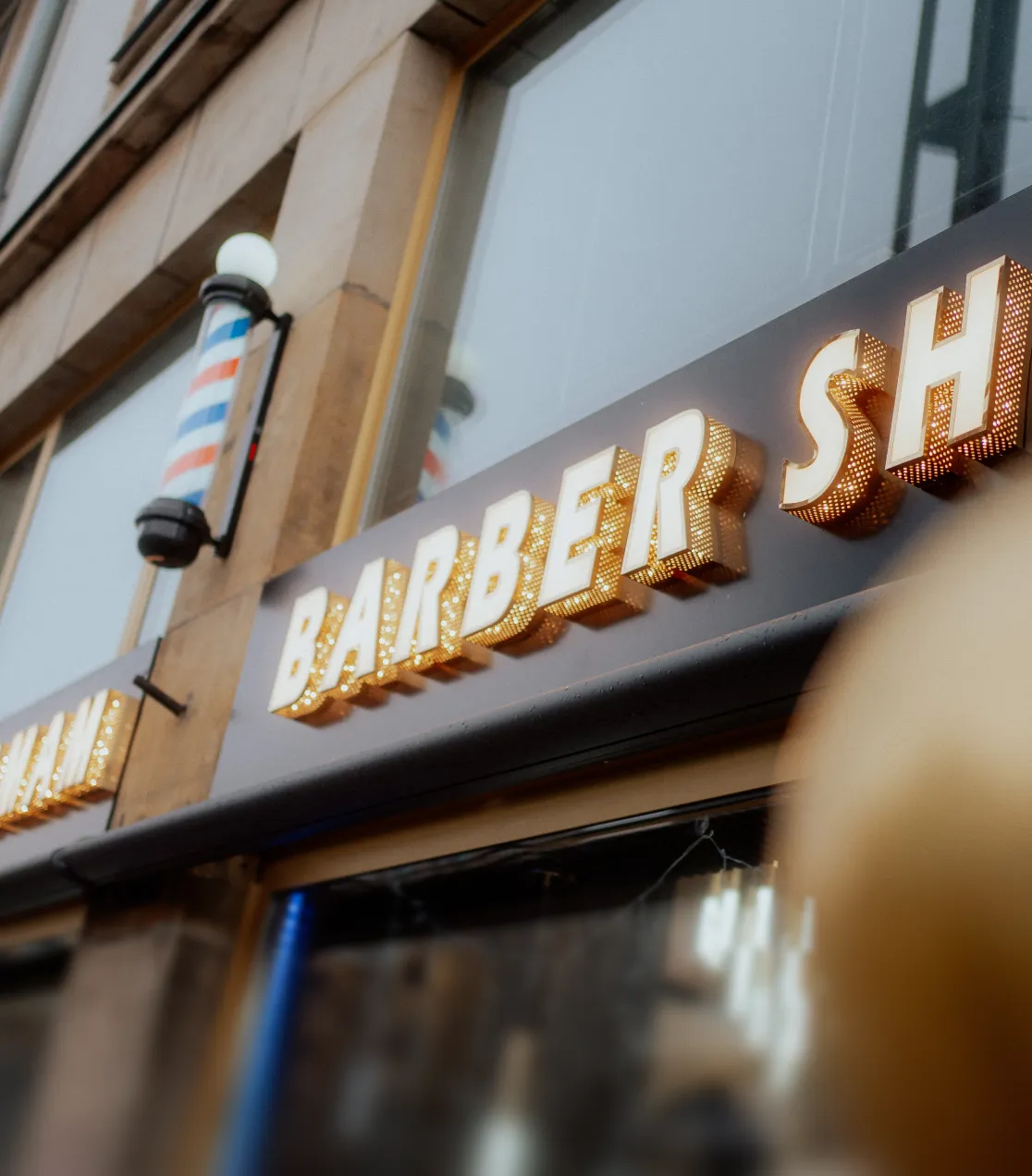 Barbershop-Fassade mit Schriftzug und klassischer Barbiersäule