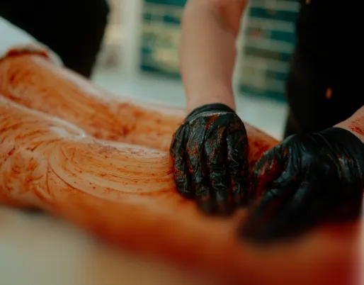 Nahaufnahme einer Ganzkörperaromatherapie mit Händen in schwarzen Handschuhen, die Kräuterpaste auf den Rücken einer Person auftragen.