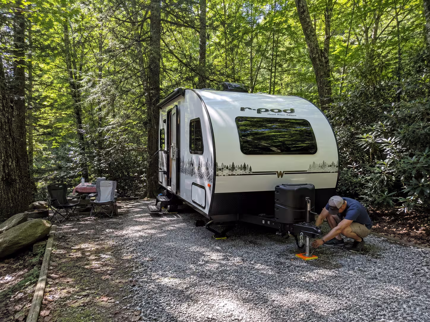 Small travel trailer on a wooded campsite pad near Asheville