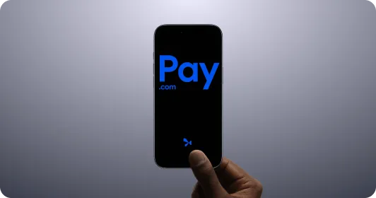 Hand holding a smartphone displaying the blue Pay.com logo on a black screen against a grey background.