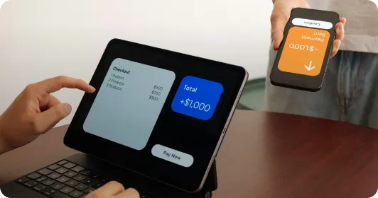 Person paying $1,000 using tablet and smartphone with contactless payment app displayed.