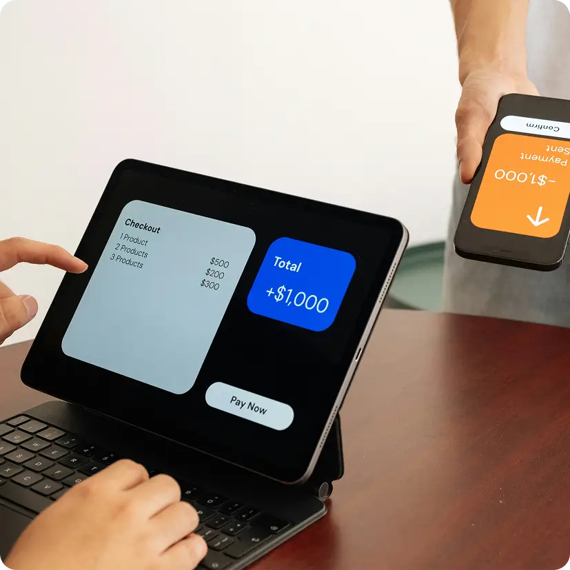 Person using tablet showing checkout screen totaling $1,000 and mobile device displaying payment confirmation.