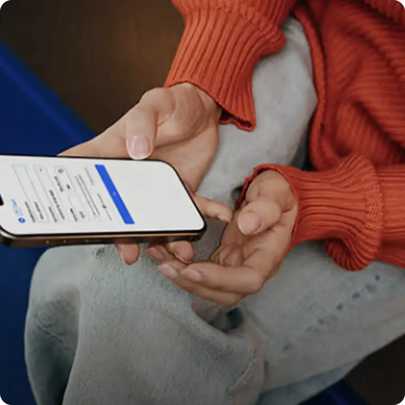 Person in red sweater holding a smartphone displaying a login screen while sitting with crossed legs.