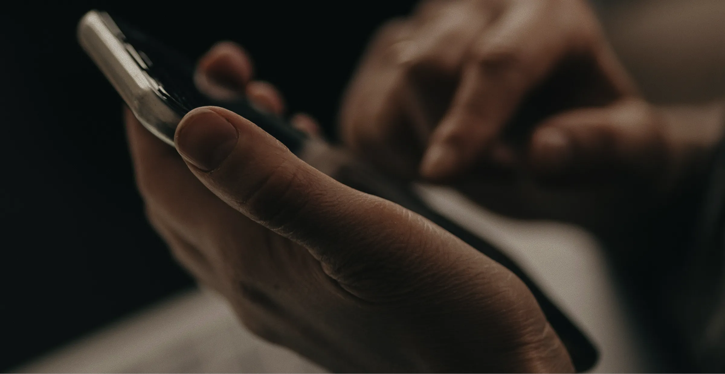 Close-up of a person holding and using a smartphone with one hand on a dark background.
