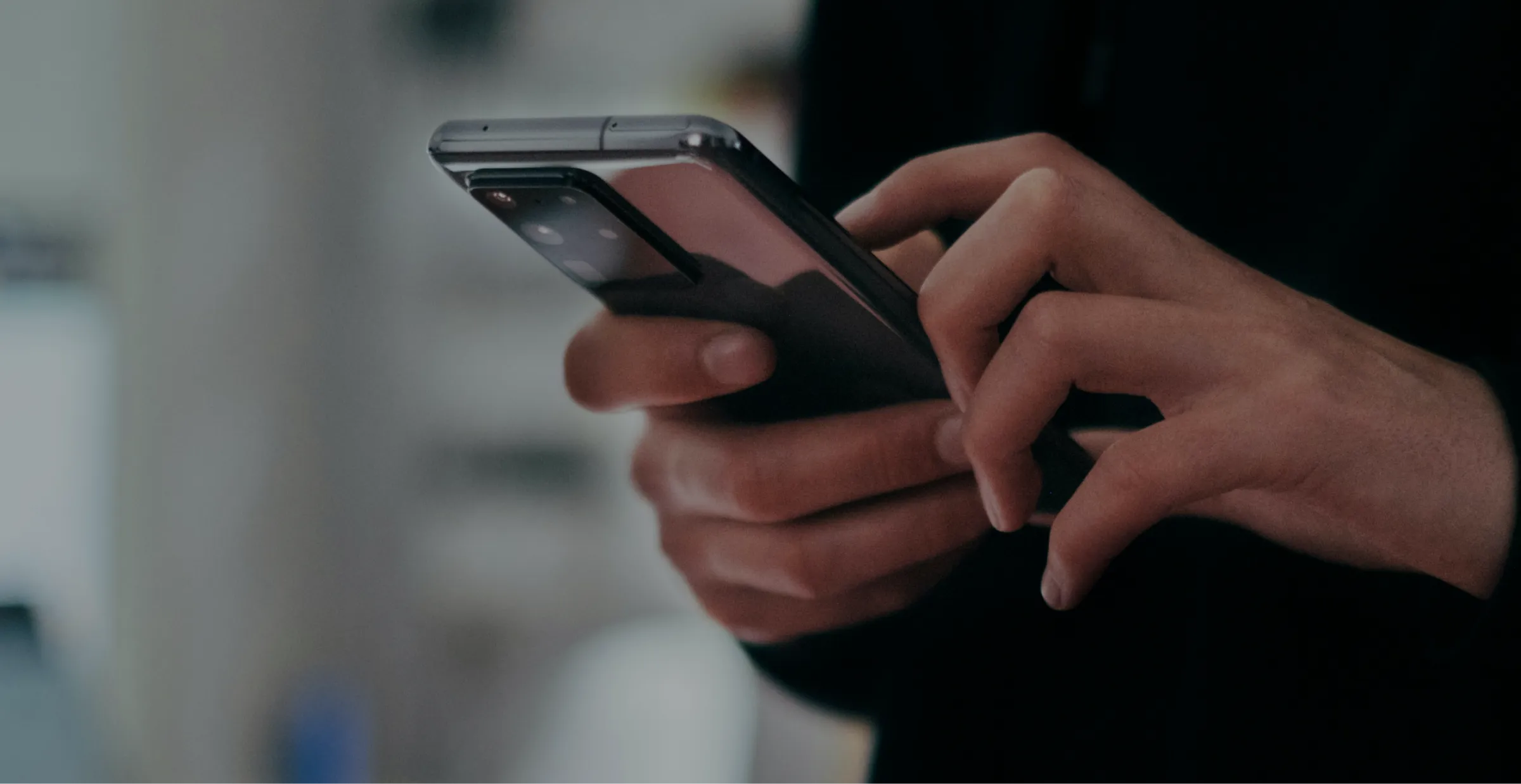 Person holding and using a smartphone with both hands in a blurred indoor setting.