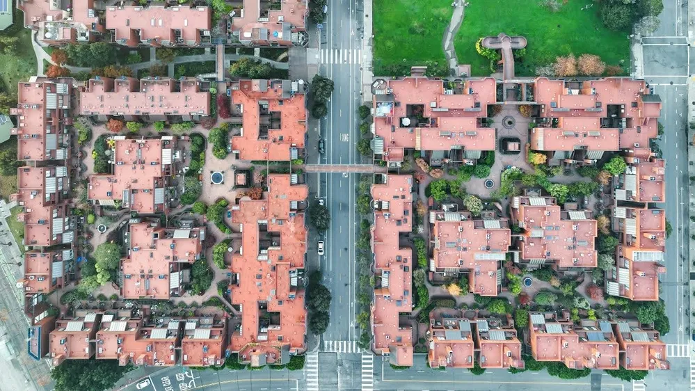 Aerial view of a residential complex with multiple buildings featuring red roofs, green landscaped areas, roads, and pedestrian crossings.