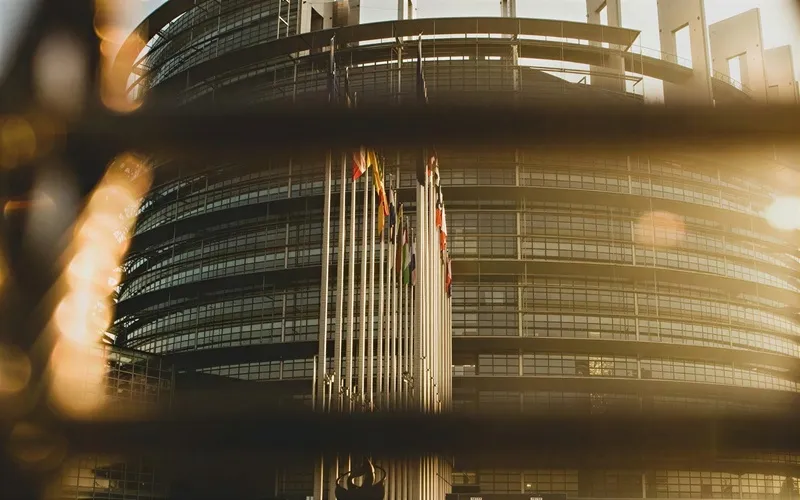Row of international flags in front of a large modern curved glass building in warm sunlight.