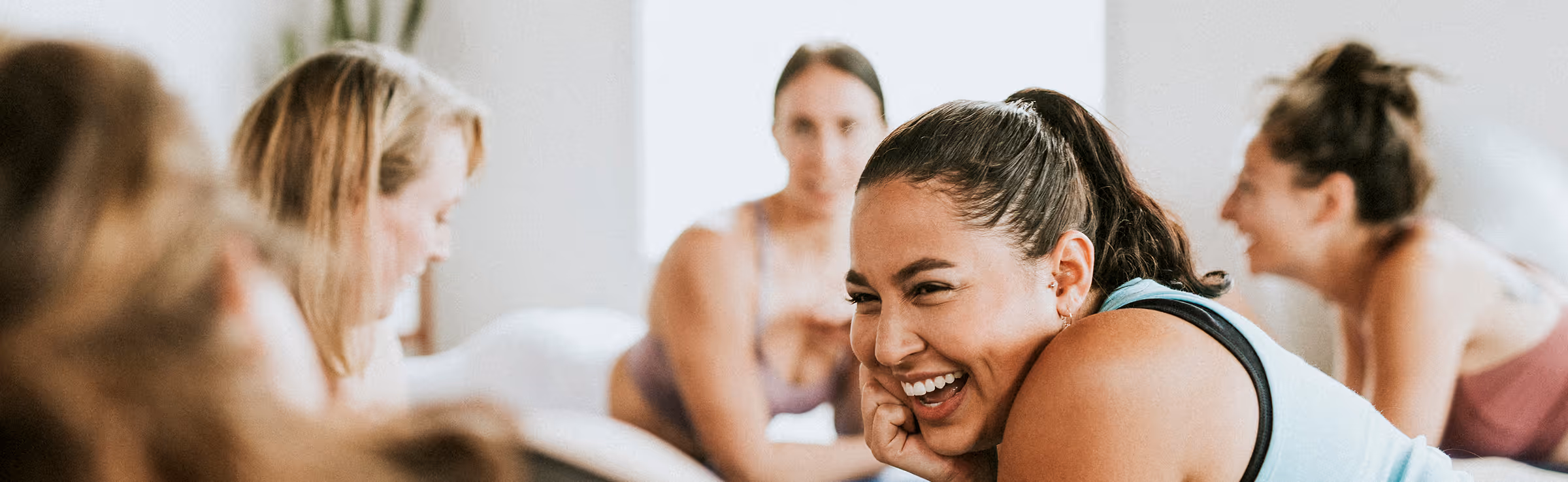 Groupe de femmes souriantes habillées en tenue de sport lors d'une séance de yoga ou d'exercice en intérieur.