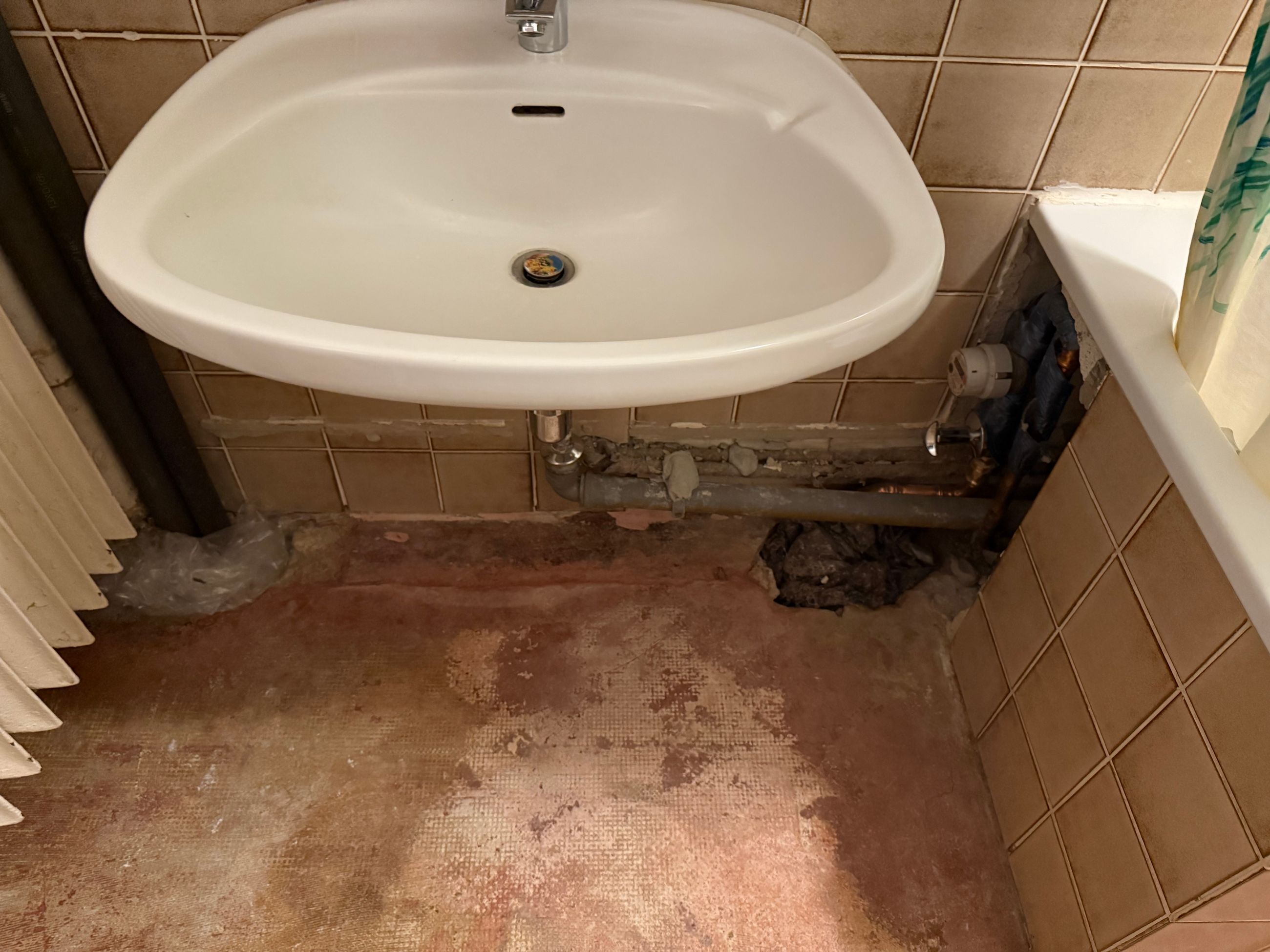 Wasserschaden im Badezimmer unter dem Waschbecken mit geöffnetem Bodenbereich vor der Sanierung