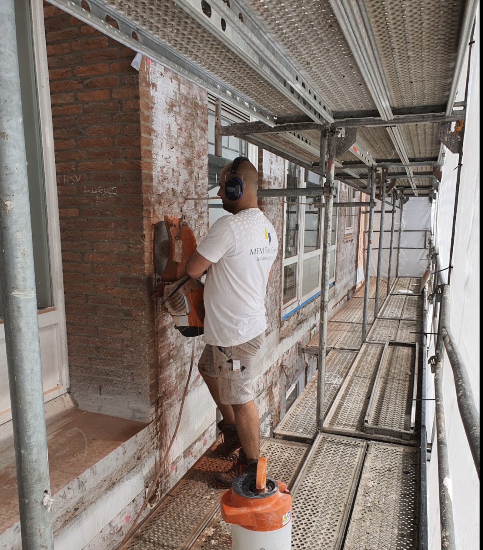 Sanierungsarbeiten an der Fassade mit Handwerker auf dem Gerüst bei der Bearbeitung einer Außenwand