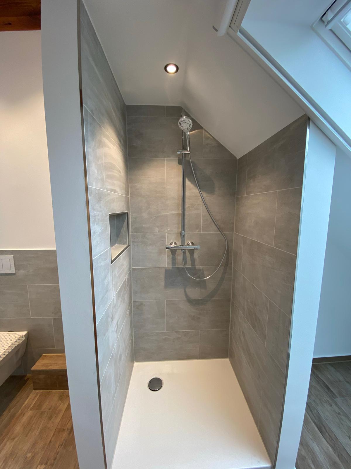 Badsanierung unter Dachschräge mit moderner Dusche, grauen Fliesen und sauberem Innenausbau