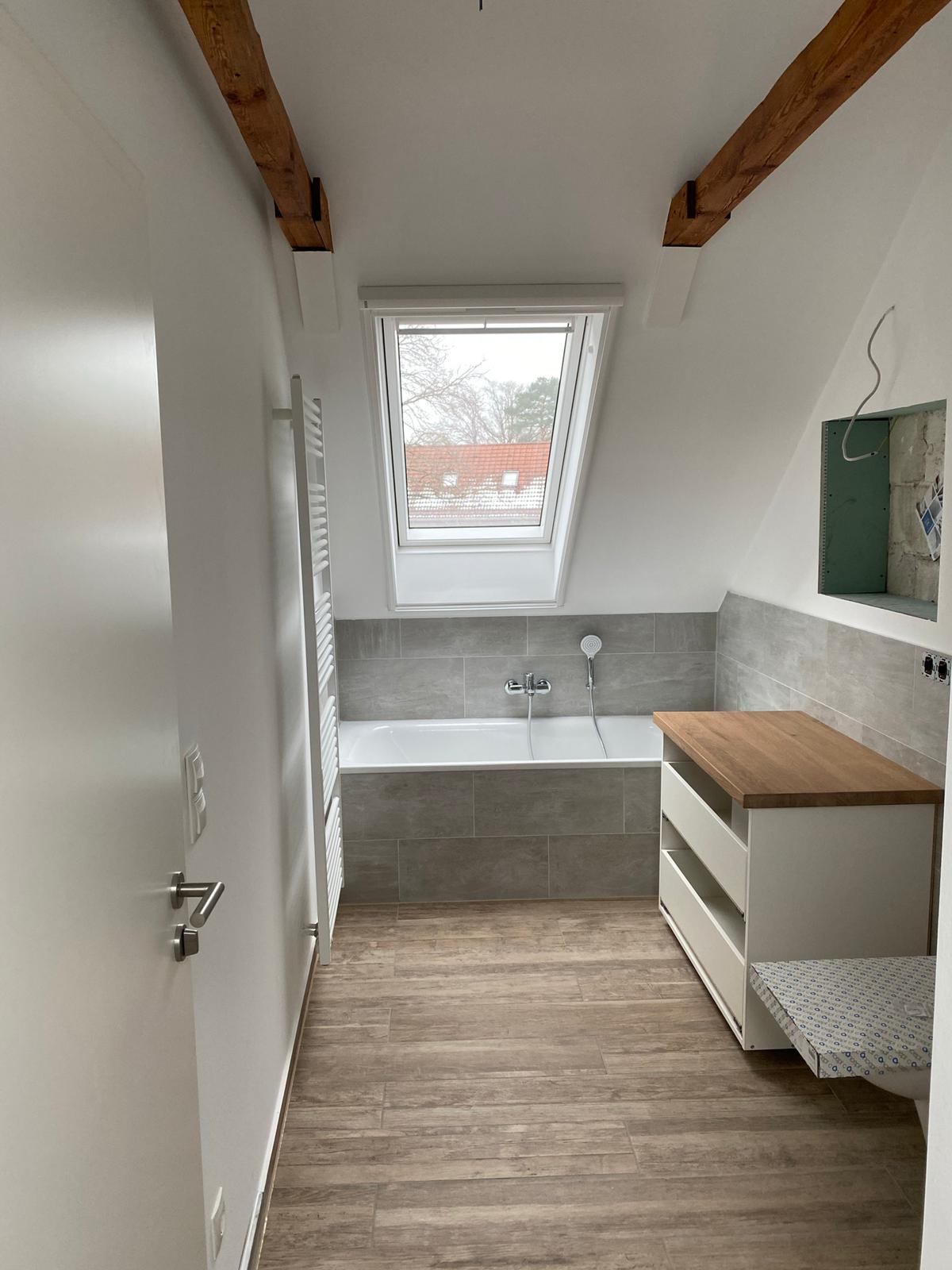 Modernisiertes Badezimmer mit Dachfenster, Waschtisch, hellen Wänden und warmem Bodenbelag