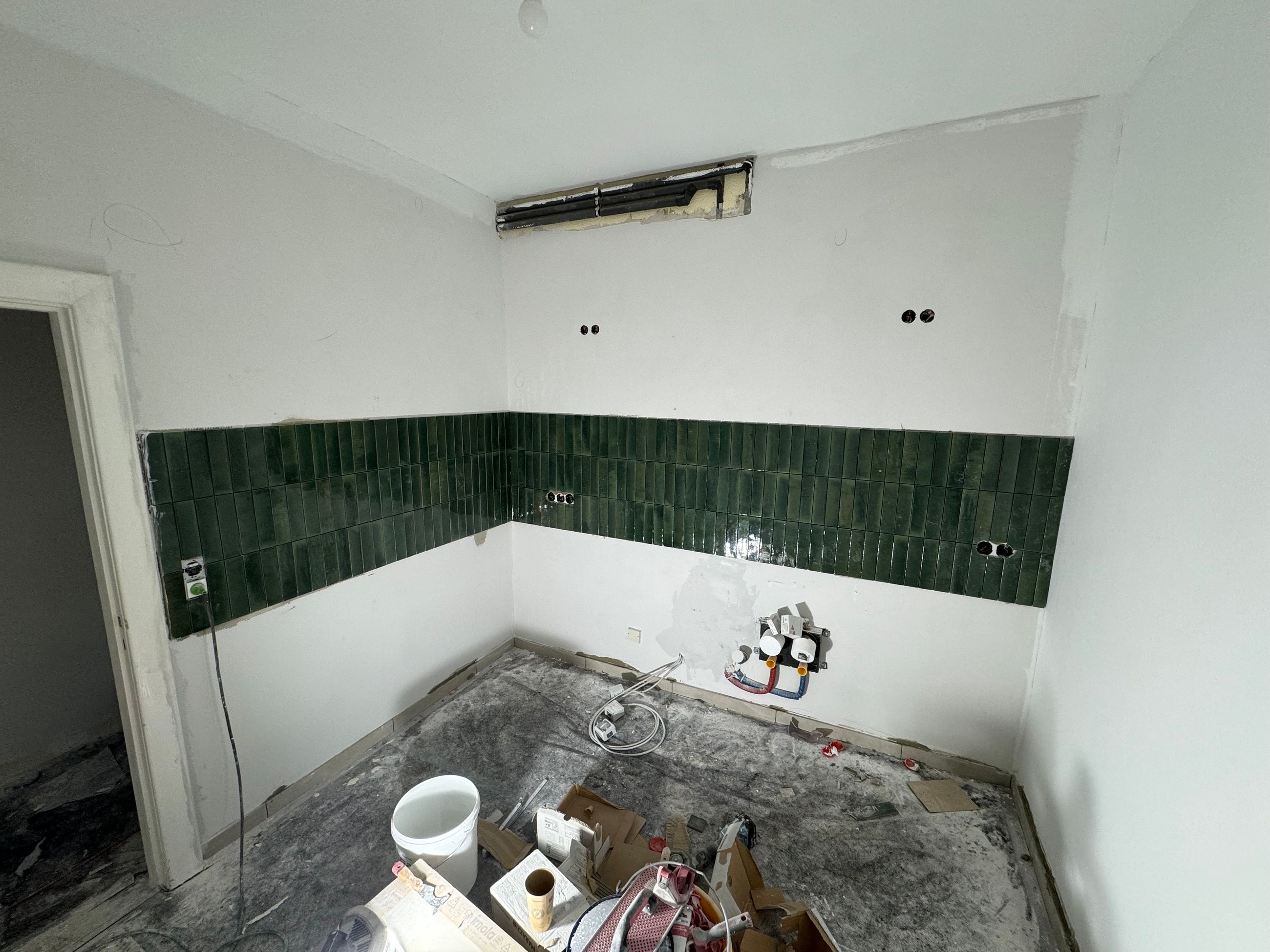 Raum mit grünen Fliesen während der Sanierung mit sichtbarer Ausbauphase im Badezimmer