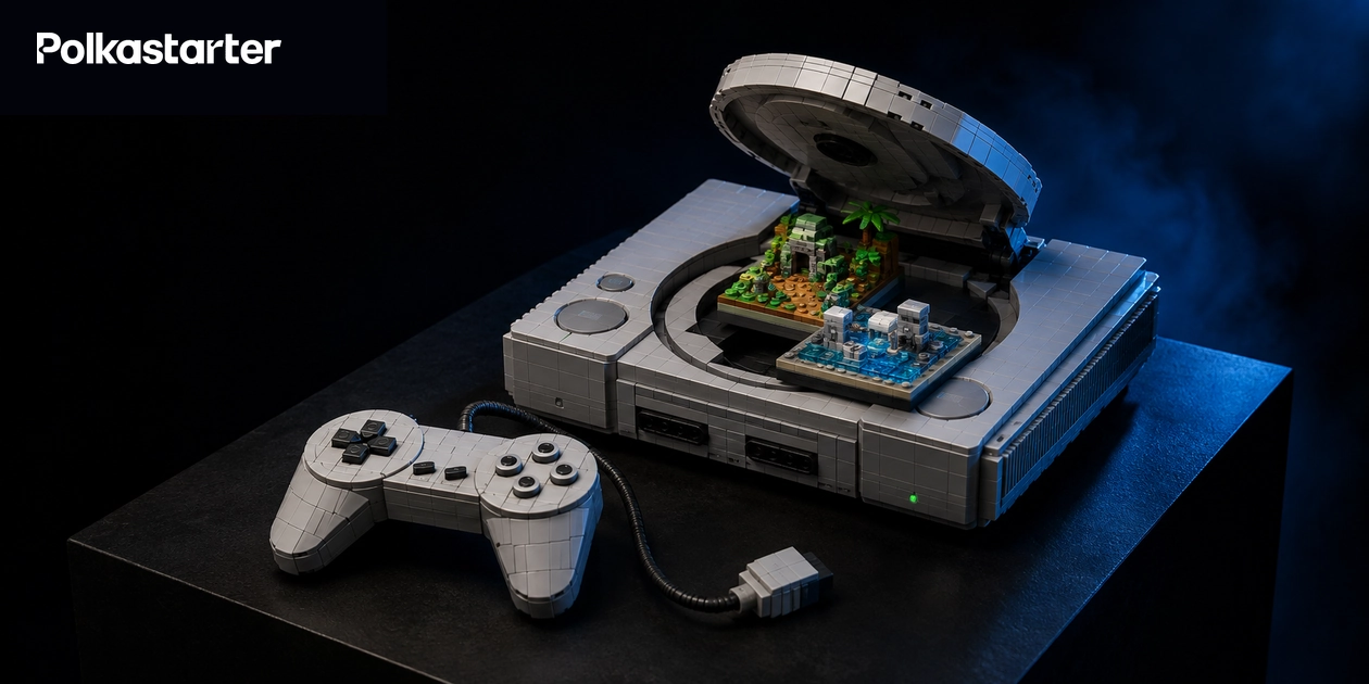 Brick-built grey original PlayStation console with its lid open over two miniature scenes and a wired brick controller on a dark display