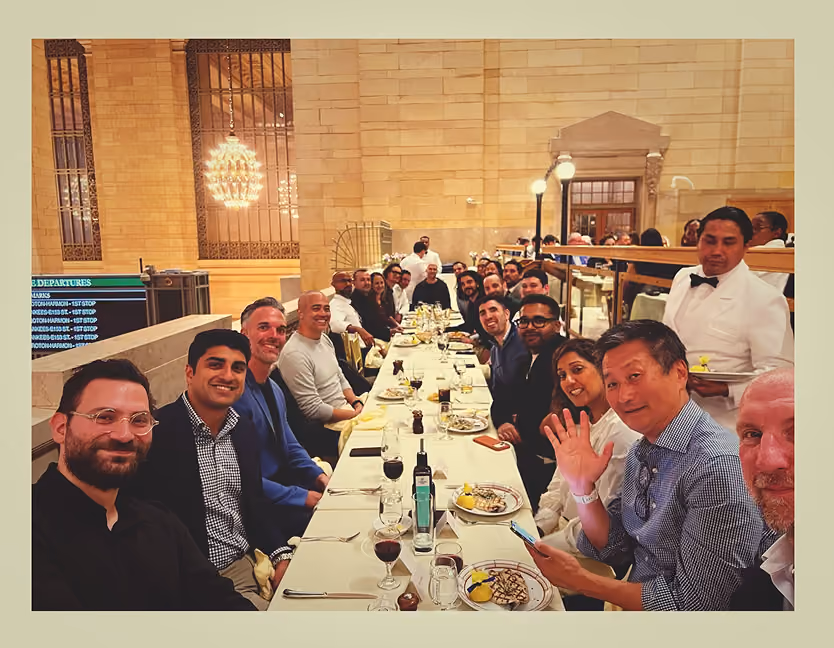 Large group seated at a long dining table in elegant restaurant with waiter serving them.