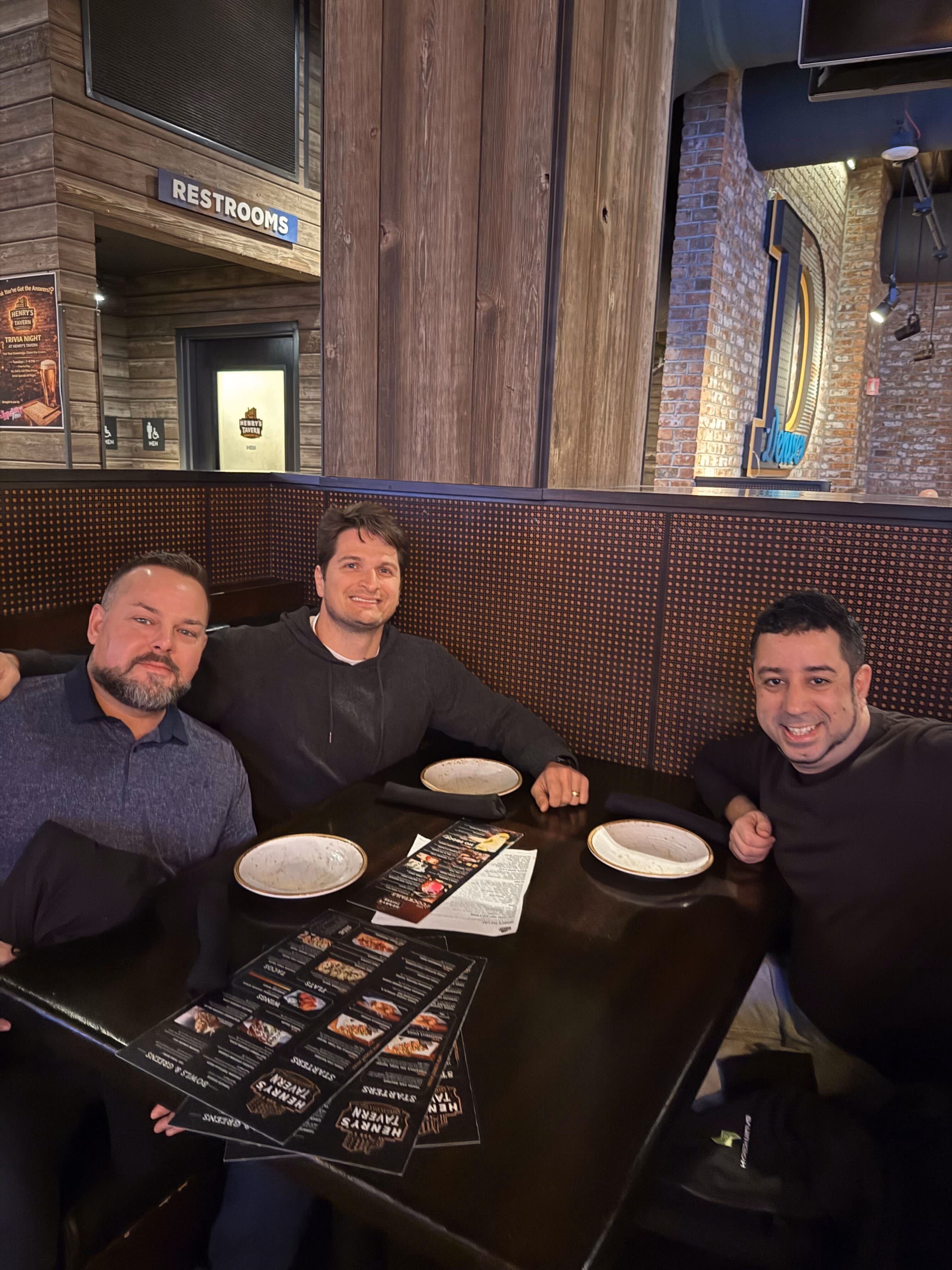 Three men sitting at a restaurant booth with menus and empty plates on the table.