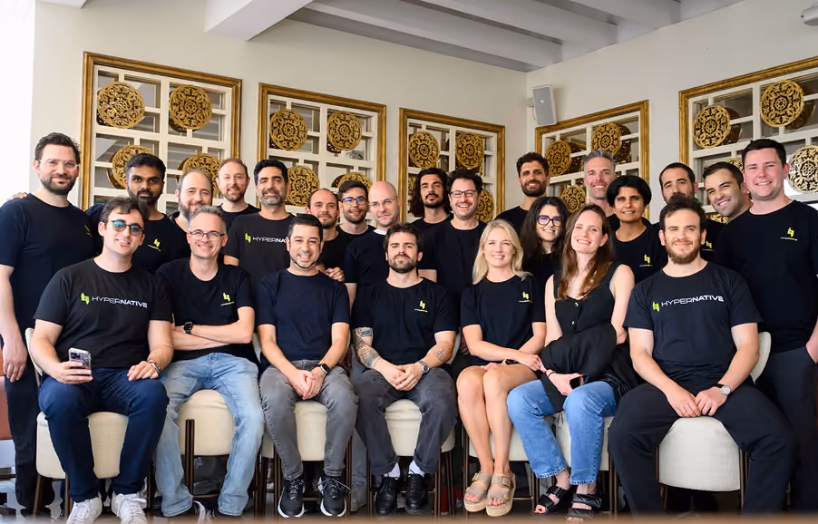 Group of 21 people, mostly wearing black 'HYPERNATIVE' shirts, posing indoors with decorative framed wall art.