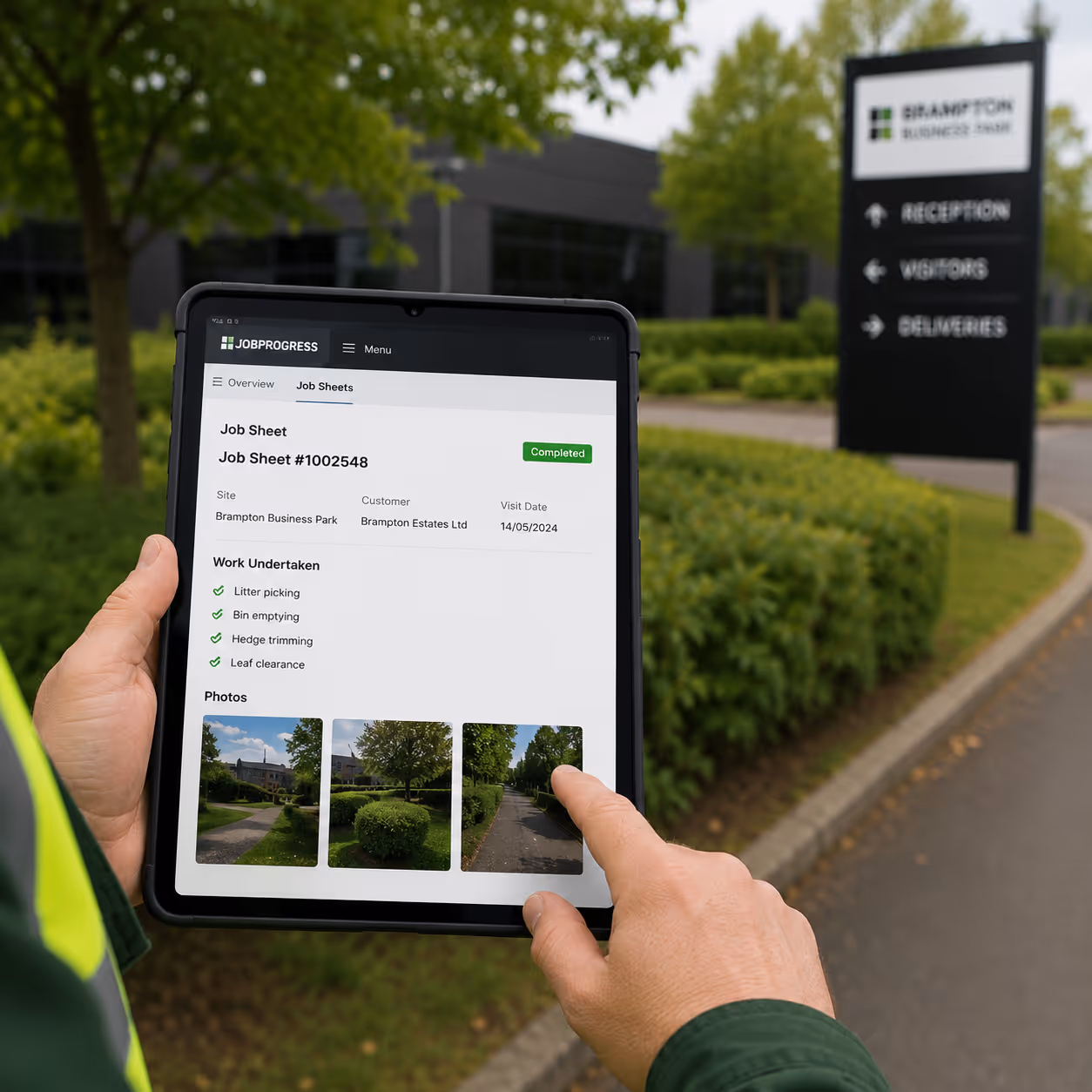 Person holding tablet displaying completed job sheet for Brampton Business Park with photos of outdoor work.