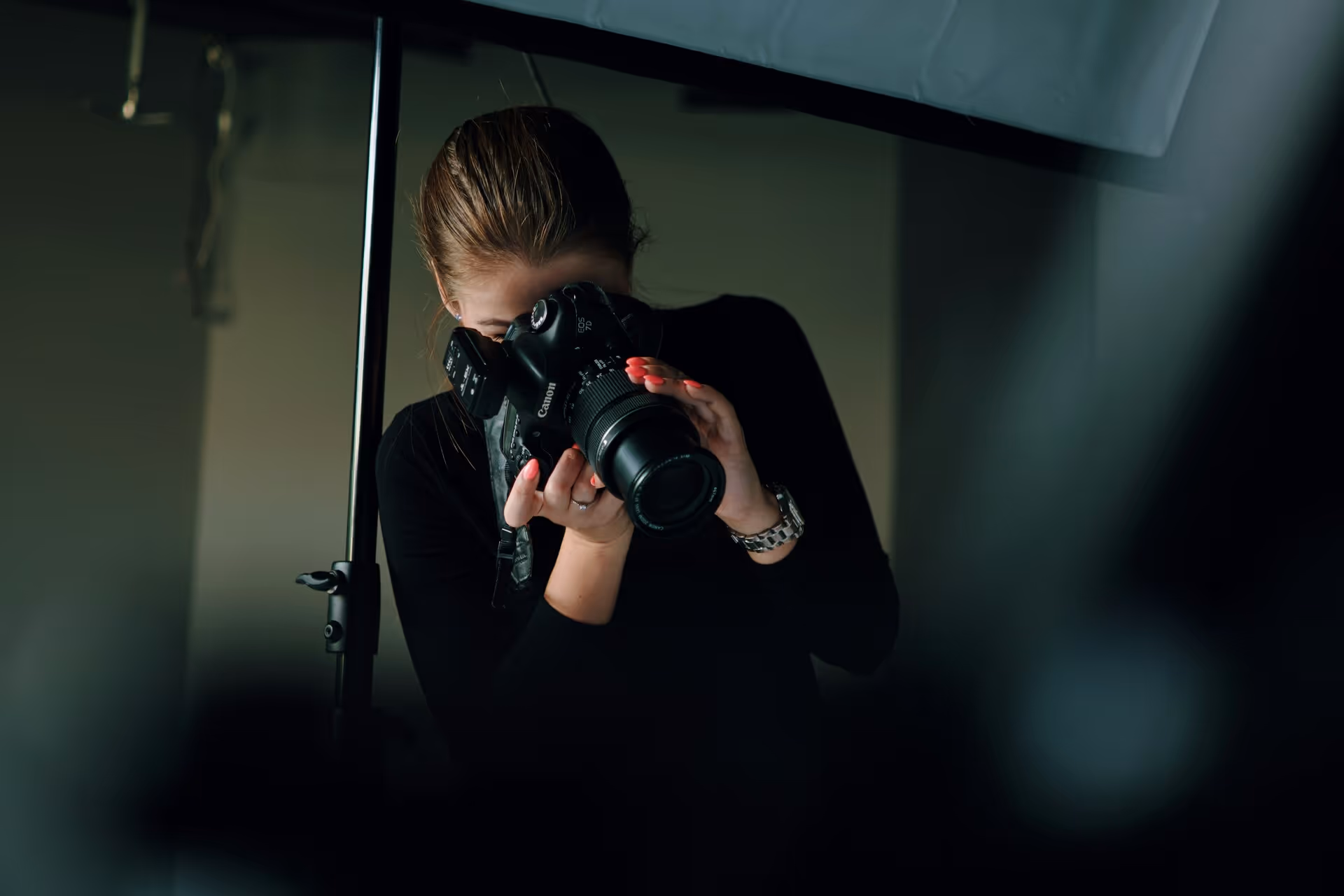 Eine Frau mit einem schwarzen Langarmshirt fotografiert mit einer Canon DSLR-Kamera in einem Studio.