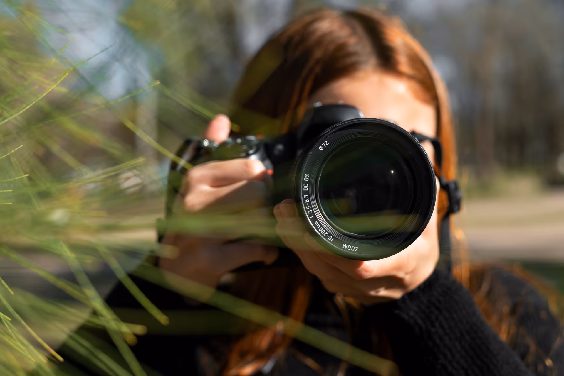 Person mit rotem Haar hält Kamera mit großem Zoom-Objektiv und fotografiert draußen.
