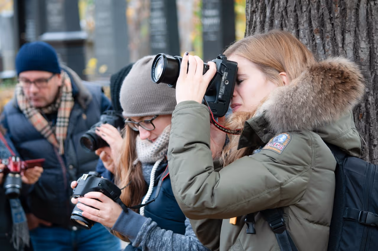 Vier Personen machen draußen mit Kameras Fotos, eine Frau lehnt an einem Baum und schaut durch die Kamera.