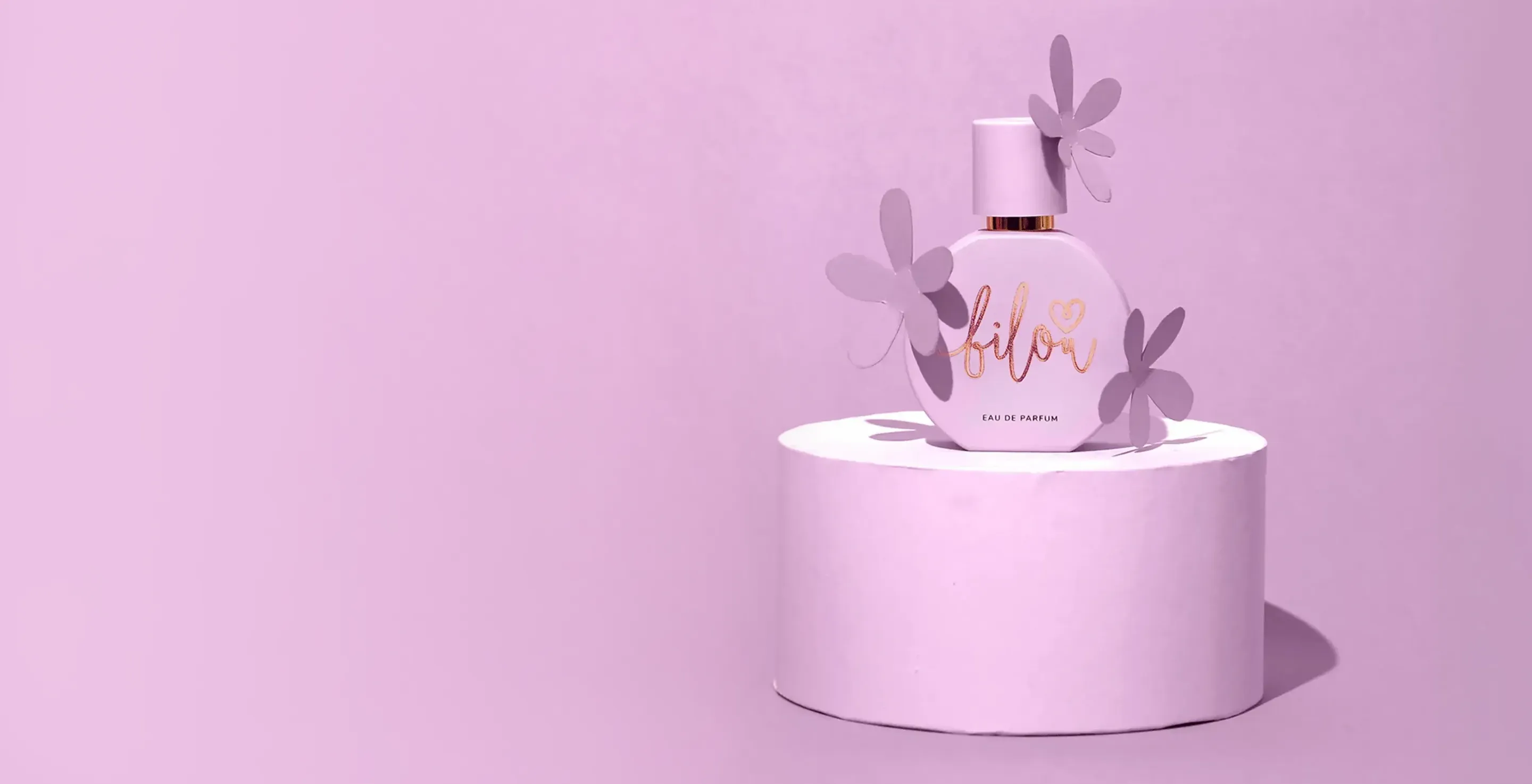 Rosa Parfümflasche mit Blumendekor auf rundem Podest vor rosa Hintergrund.