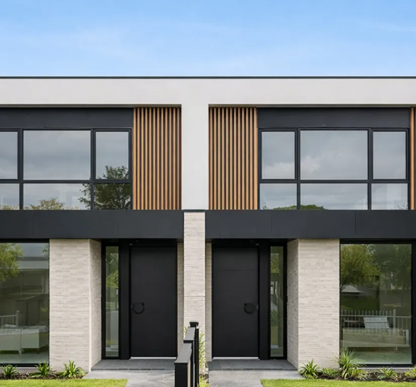 Front view of a modern duplex with black doors, large windows, beige brick columns, and vertical wooden slats.