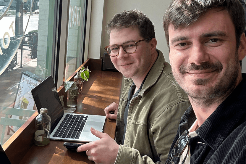 Two Neurolabs colleagues smiling at a cafe window bench with an open laptop