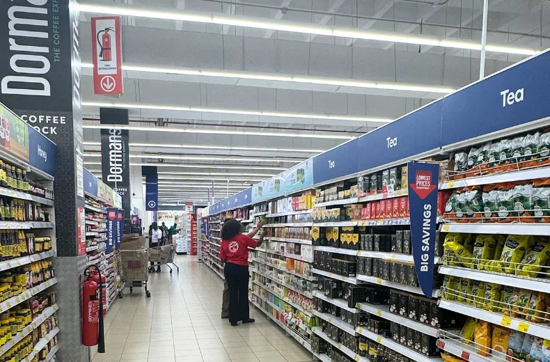 Tea and coffee aisle of a Kenyan supermarket with a staff member facing up stock under Dormans and Tea signage