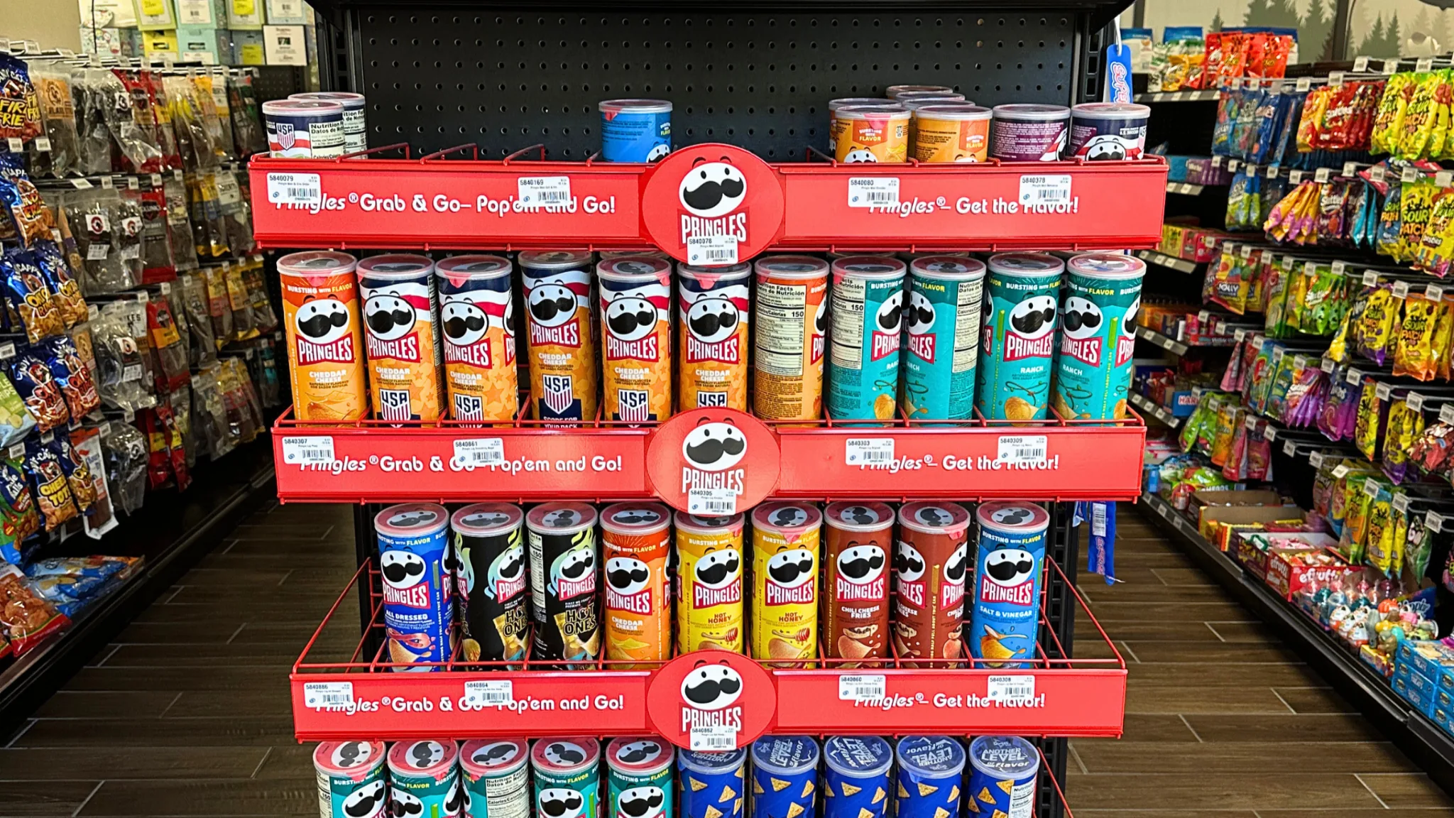 Three-tier Pringles Grab & Go display packed with crisp cans between snack aisles in a convenience store