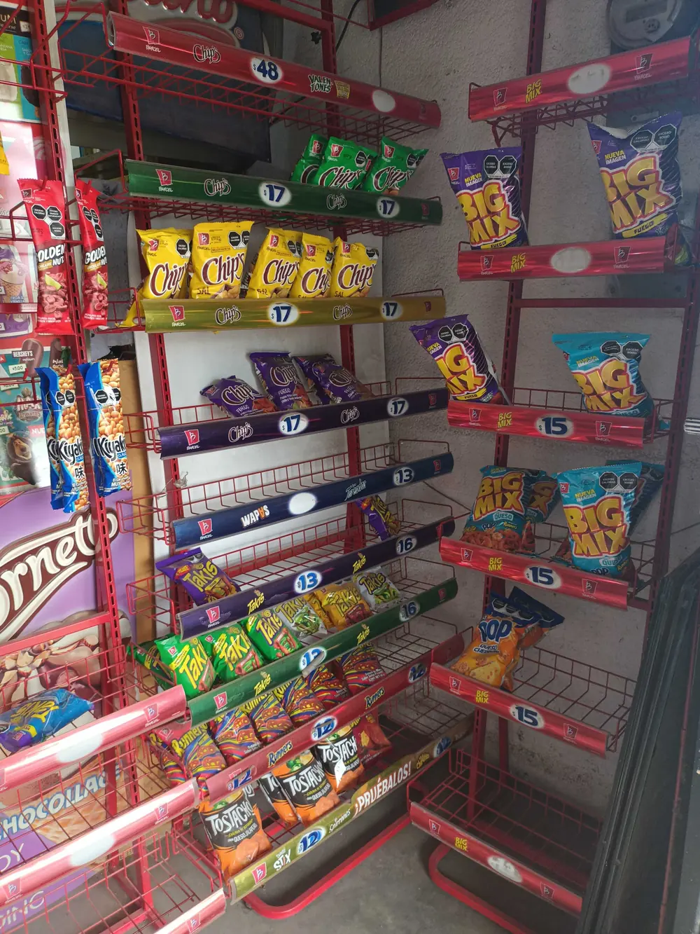 Angled field photo of a red wire snack rack in a small store, with price strips partly cut off.