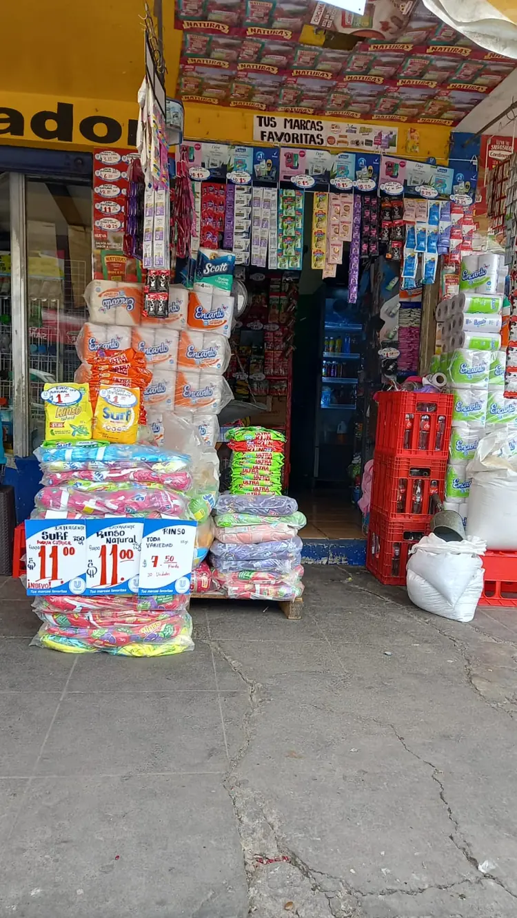 Small independent shopfront in Latin America with snacks, drinks and household goods stacked around the doorway.