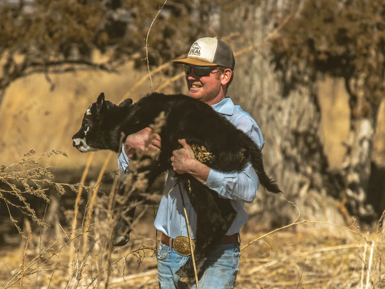 rancher holding a calf in pasture