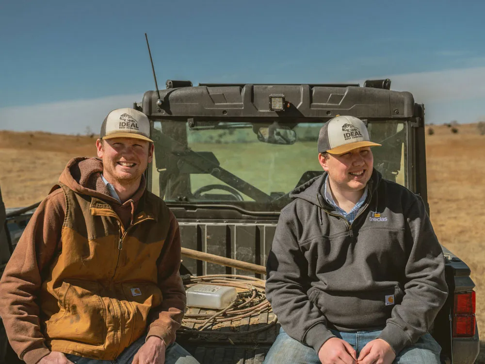two ranchers sitting in front of utility vehicle on ranch