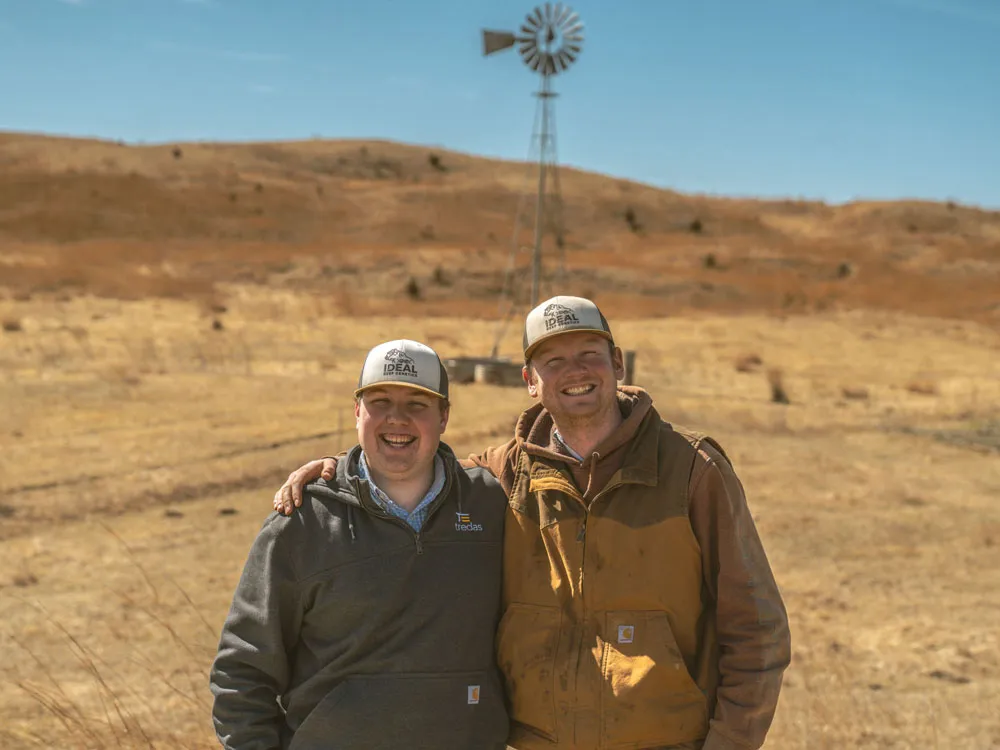 two ranchers standing together in pasture with windmill in background