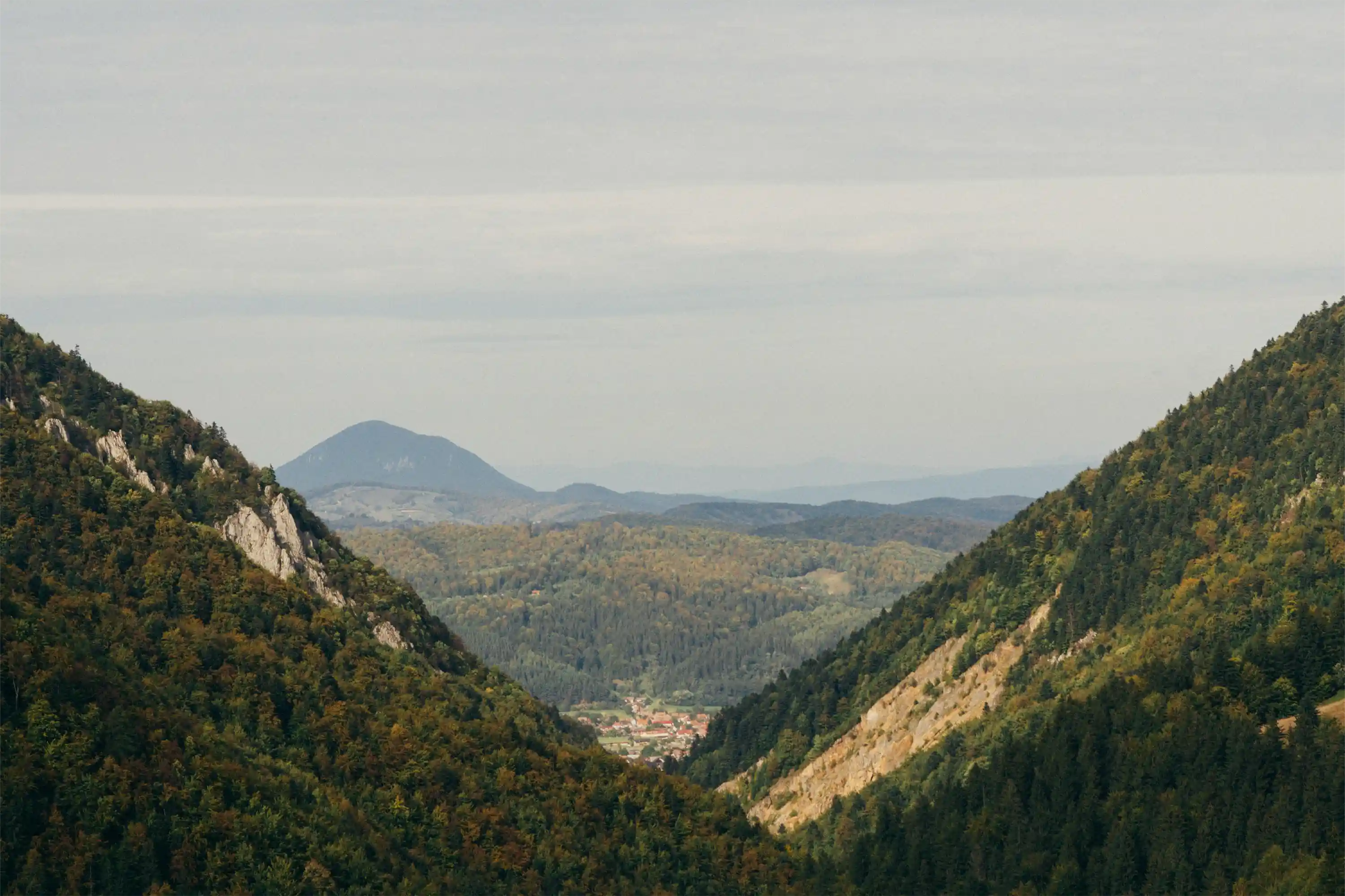 Valley between two forested mountains with distant hills and a village visible in the center.