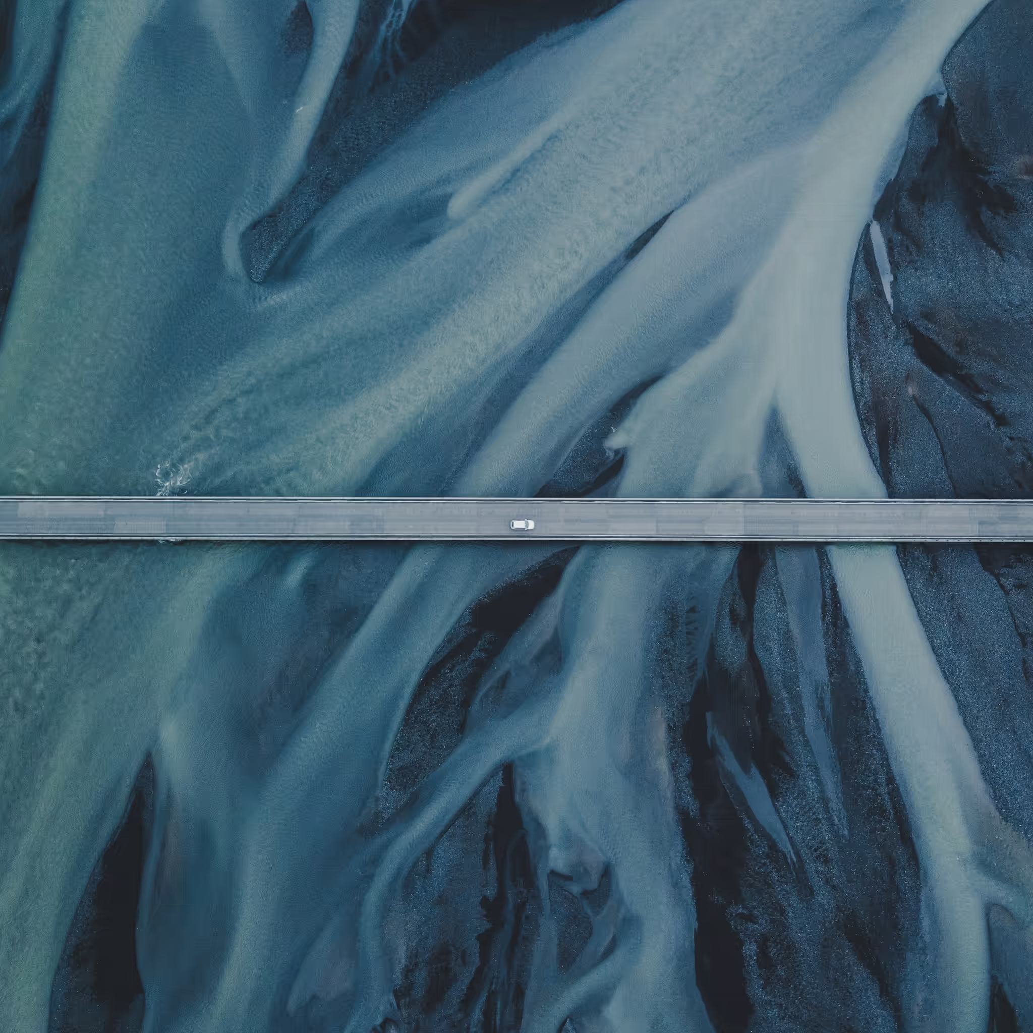 Aerial view of a bridge crossing over river channels with a single white car driving on it.