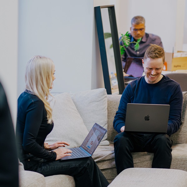 Two people sitting on a couch working on laptops.