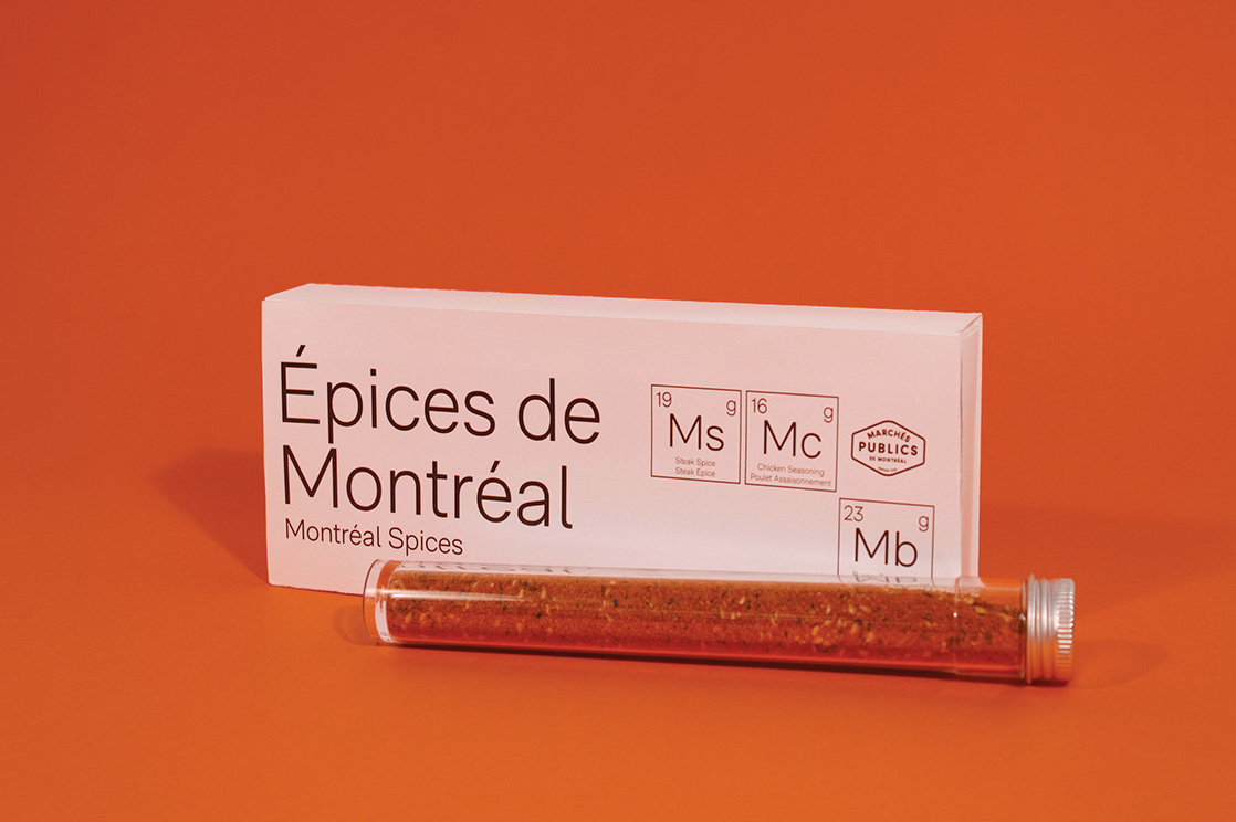 Front picture of the new MPM product, Spices of Montreal against an orange background with the steak spice container laying down in front of the packaging.
