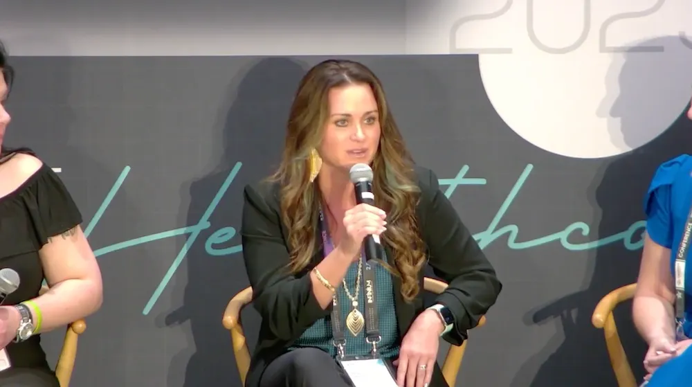 Woman with brown hair speaking into microphone at panel discussion on stage