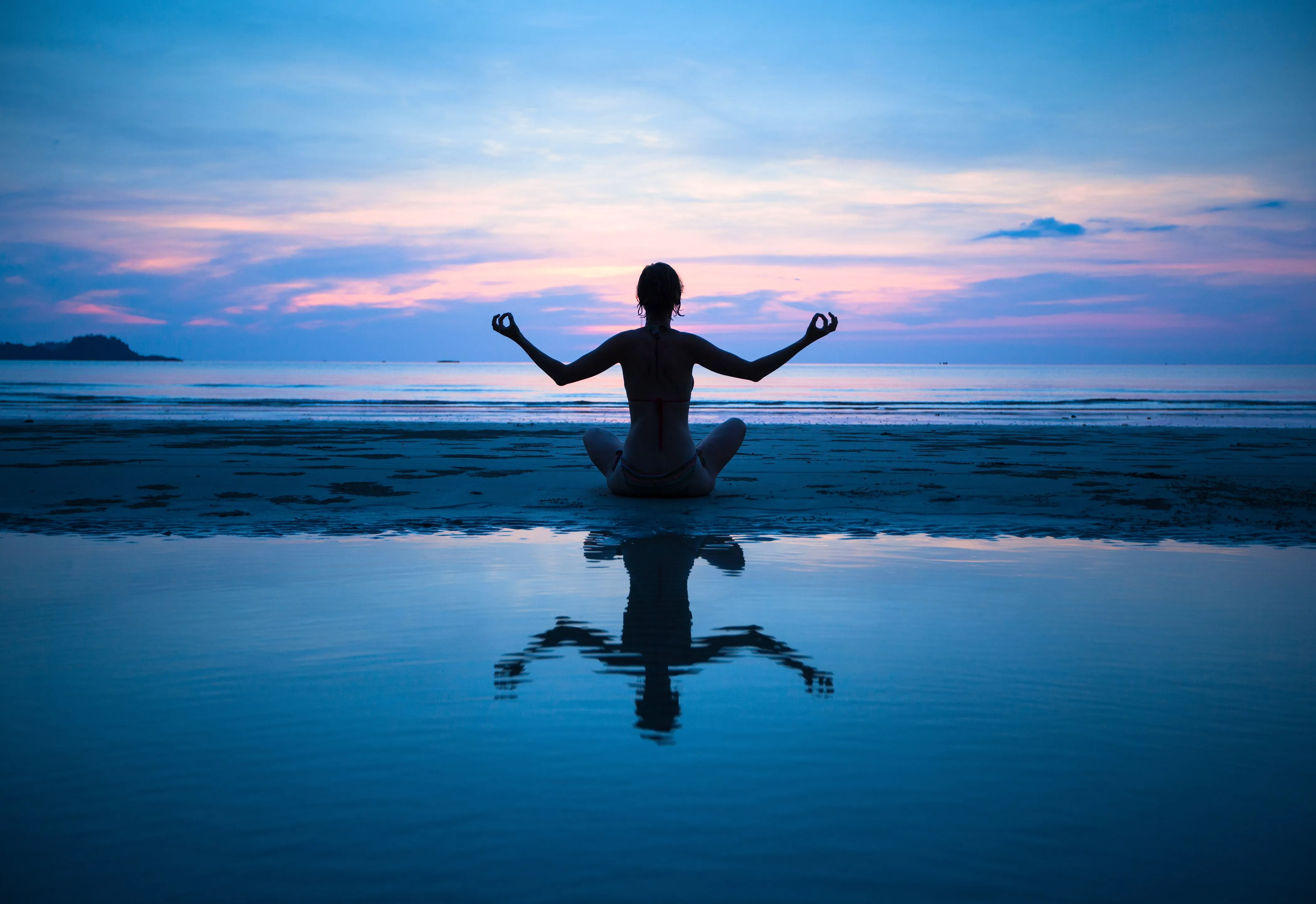 Silhouette of person meditating on beach at sunset with arms raised peacefully
