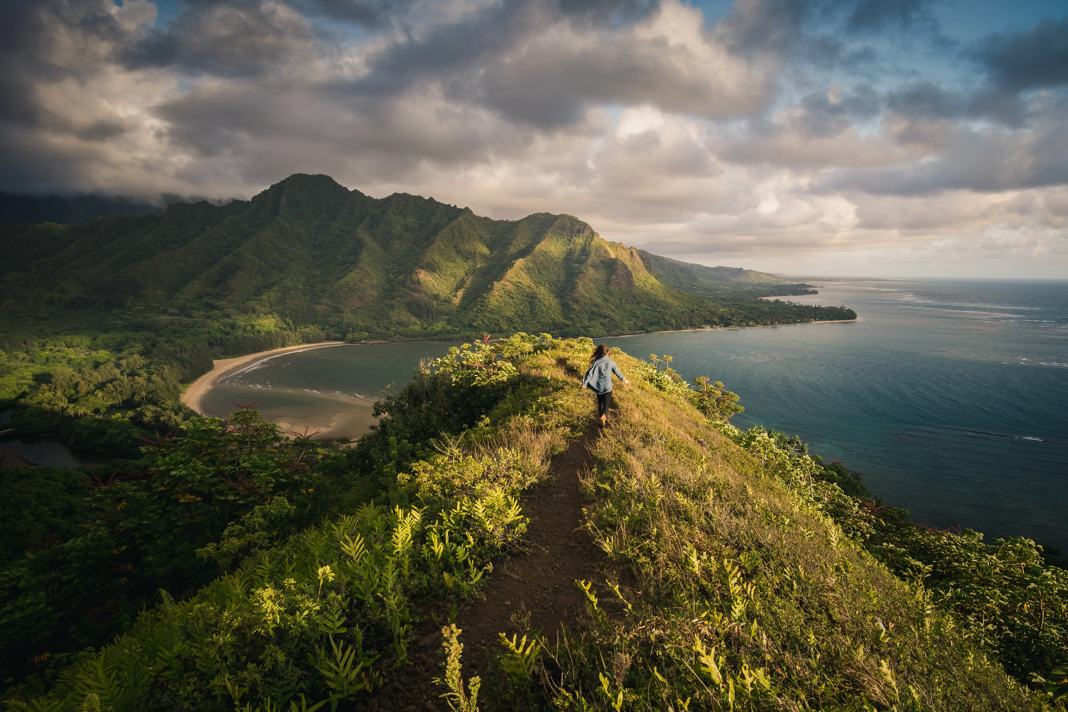 Hiker standing on cliff overlooking tropical bay and green mountains with ocean