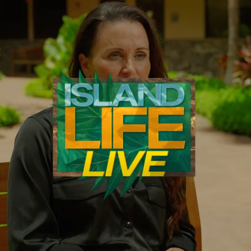 Woman holding Island Life Live sign with green foliage background outdoors
