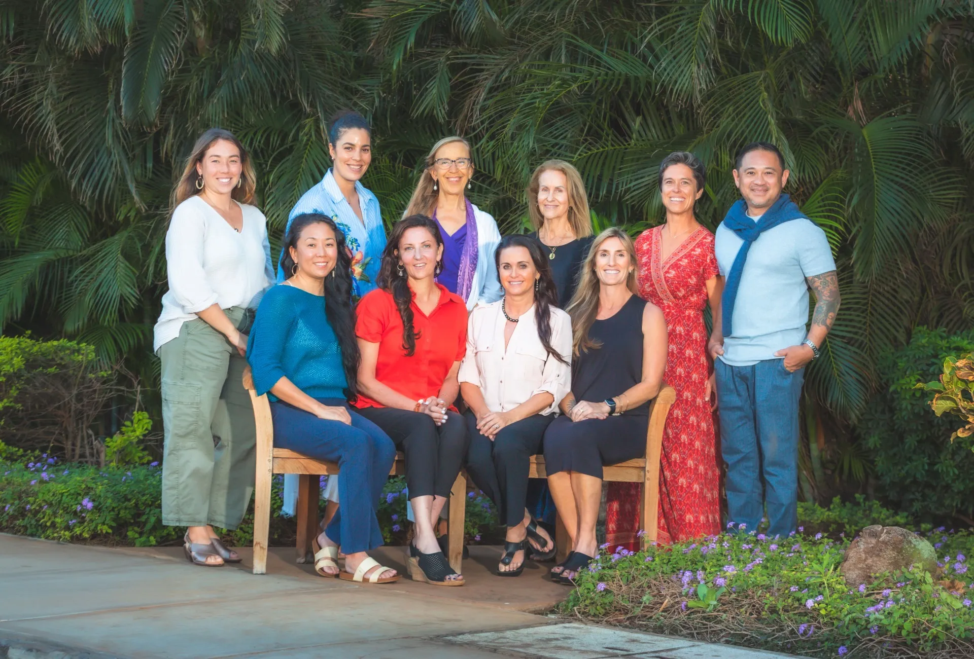 Group of eleven diverse people posing together in tropical garden setting with palm trees.